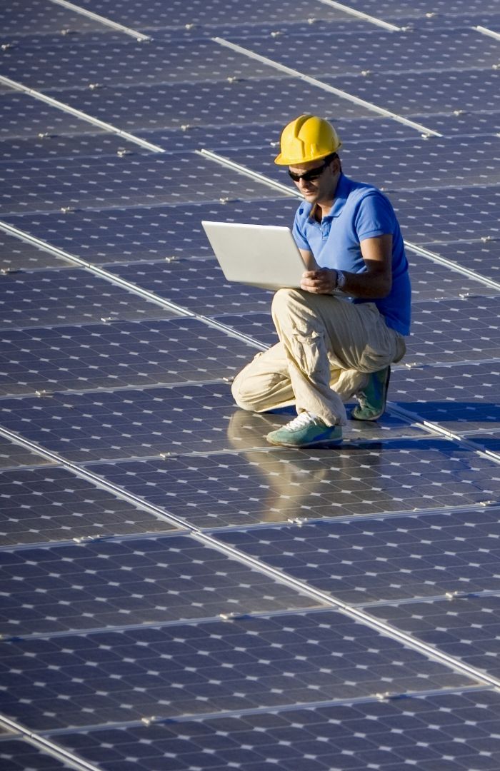 A male technician checking their laptop on top of solar panels